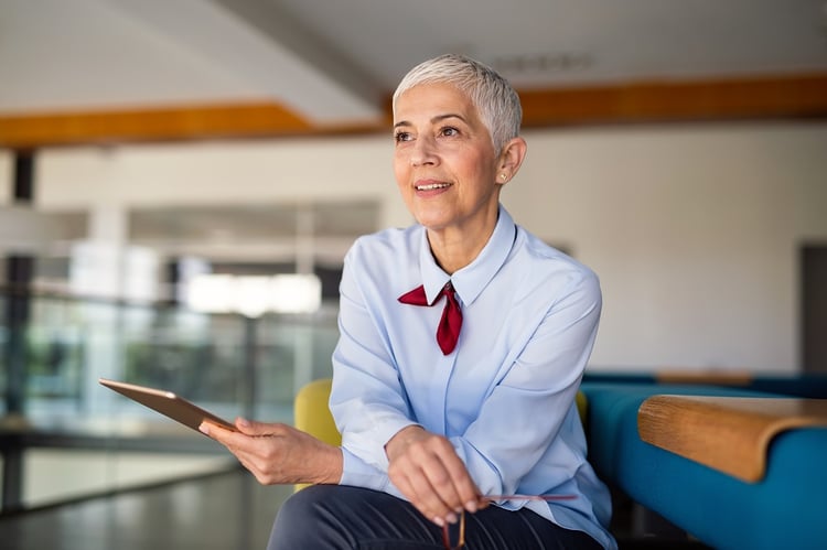 Apps and Automation in Microsoft 365 | Woman in blue shirt sits on a couch in an office, holding a tablet 