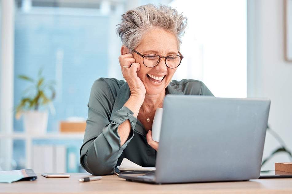 Woman simling at her laptop holding a coffee cup | Improve digital skills at scale across your organisation