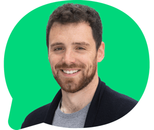 Headshot of Nathan Rhodes (male, brown beard, wearing a black cardigan) smiling at the camera. In a green bubble graphic frame.