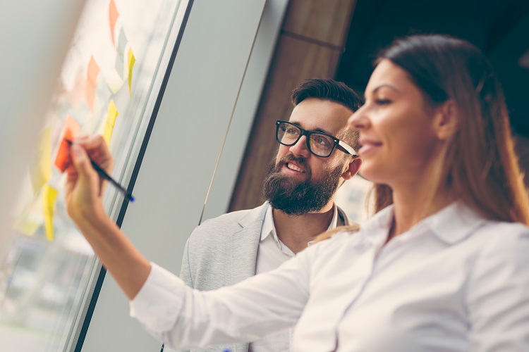 Two colleagues looking at a planning whiteboard, smiling | Cloud Migration Planning Two colleagues looking at a planning whiteboard, smiling | Cloud Migration Planning