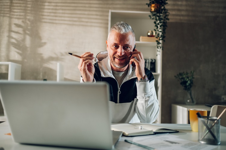Man sits at his laptop, while on the phone | Microsoft 365 Governance Man sits at his laptop, while on the phone | Microsoft 365 Governance